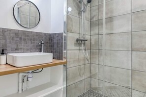 Ein Badezimmer mit einem weißen Waschbecken, einem Spiegel und einem Duschbereich mit gefliesten Wänden.
