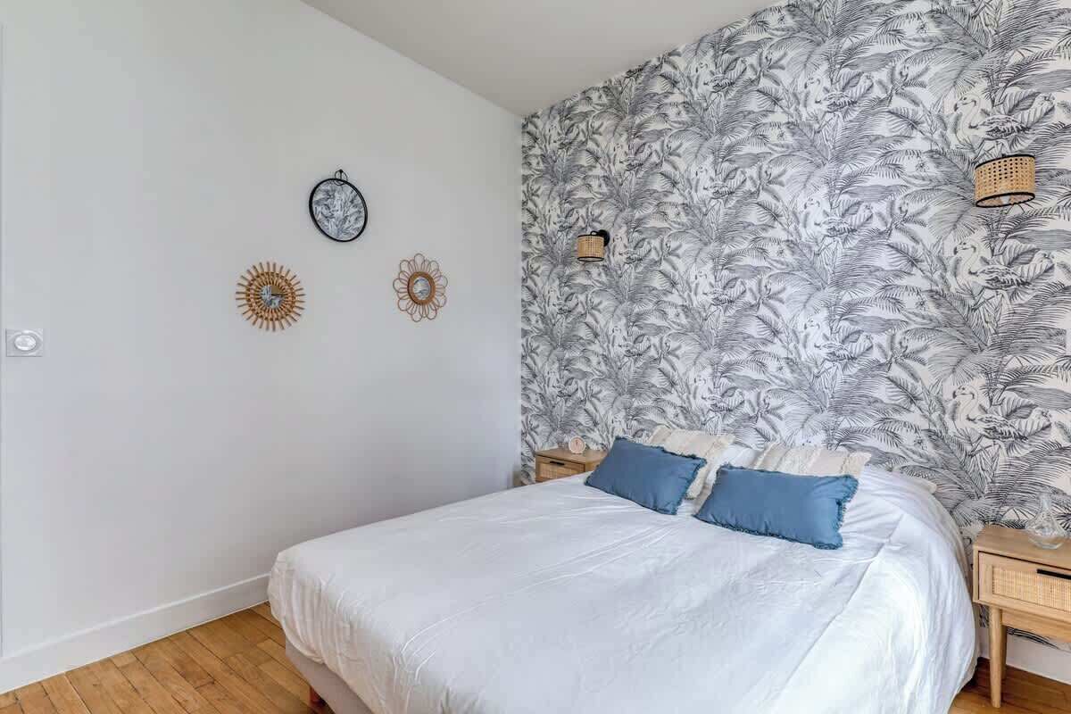 A bedroom with a bed, two nightstands, a wall clock, and a floral wallpaper.