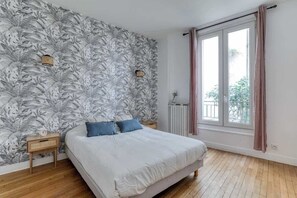 A bedroom with a large bed, a window with curtains, a radiator, and a wall with a leaf pattern. - Poissonnière – Cosy Apartment near Montmartre (Paris)