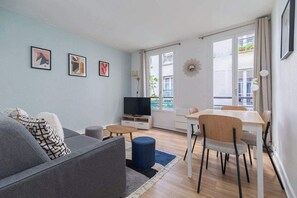 A modern living room with a sofa, a TV, a dining table with chairs, and artwork on the wall. - Greneta - Spacious Flat Montorgueuil 4PAX (Paris)