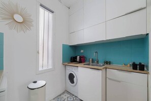 Een kleine keuken met een wasmachine, een spoelbak en een raam.