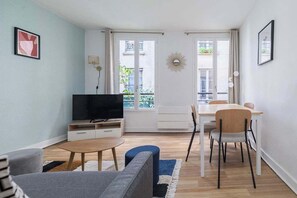 A living room with a TV, sofa, dining table, chairs, and a balcony view. - Greneta - Spacious Flat Montorgueuil 4PAX (Paris)