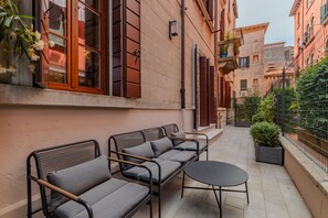 Et udendørs opholdsområde med sofa og bord, en potteplante og en bygning med balkon.