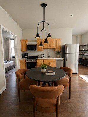 A modern kitchen with wooden cabinets, a stainless steel refrigerator, and a dining area with a round table and chairs. - Modern 2BR in Heart of Philly | Rafa Properties (Philadelphia)
