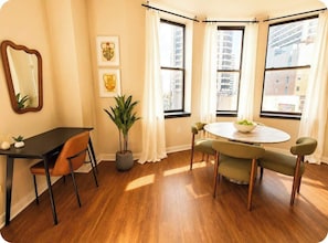 A corner room with a dining table, chairs, a potted plant, and a window with curtains. - Spacious 2BR Center City Gem | By Rafa Properties (Philadelphia)