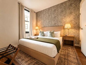 A hotel room with a bed, two bedside lamps, a wooden bench, and a patterned rug. - Beautiful 2BR Center City Gem | By Rafa Properties (Philadelphia)