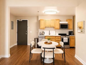 A modern kitchen with wooden cabinets, a central island, and a dining area with four chairs. - Beautiful 2BR Center City Gem | By Rafa Properties (Philadelphia)