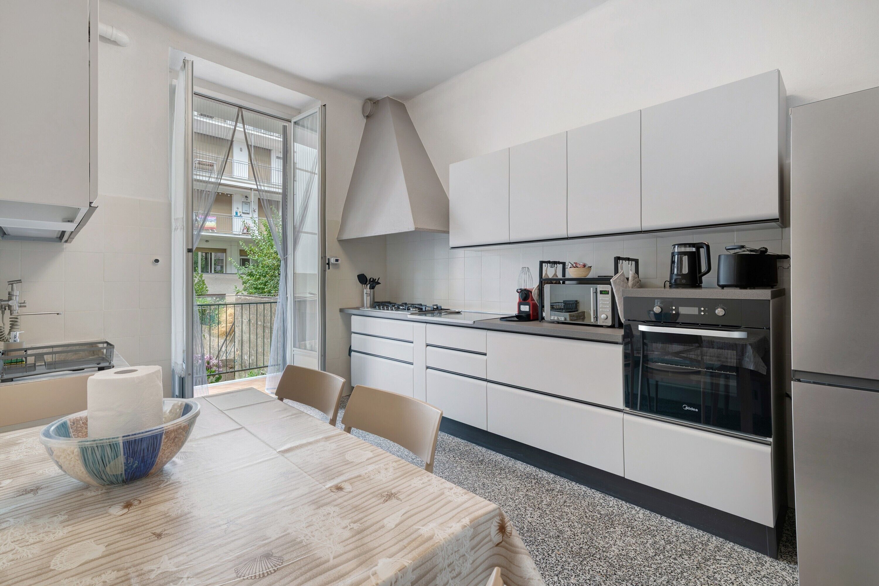 Una cucina moderna con mobili bianchi, un tavolo da pranzo con sedie e vista sull'esterno tramite una porta vetrata.