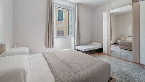 Ett hotellrum med en säng, ett litet sängbord, en spegel och ett fönster med gardiner.