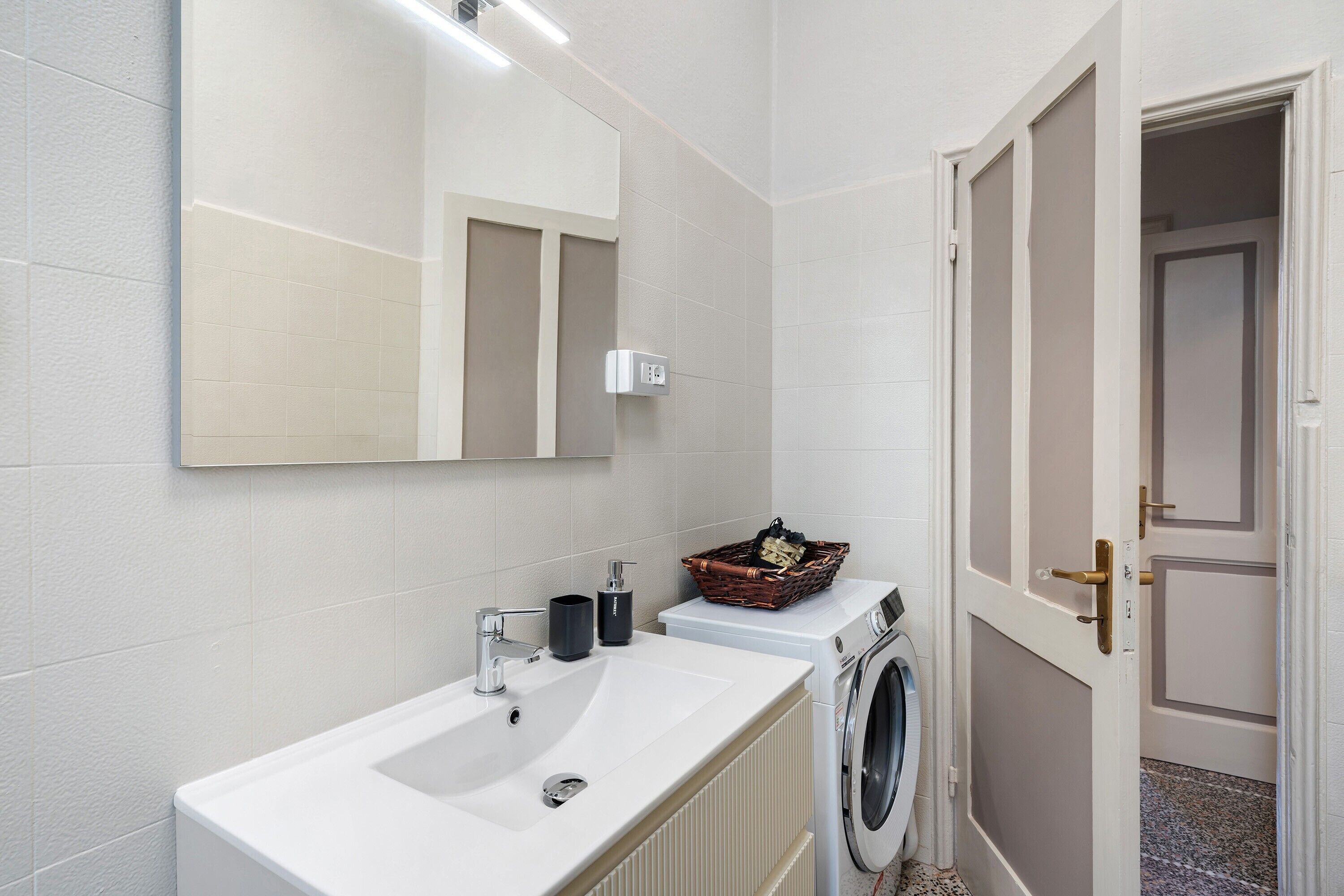 Un baño con un lavabo blanco, un espejo, una lavadora y una puerta.