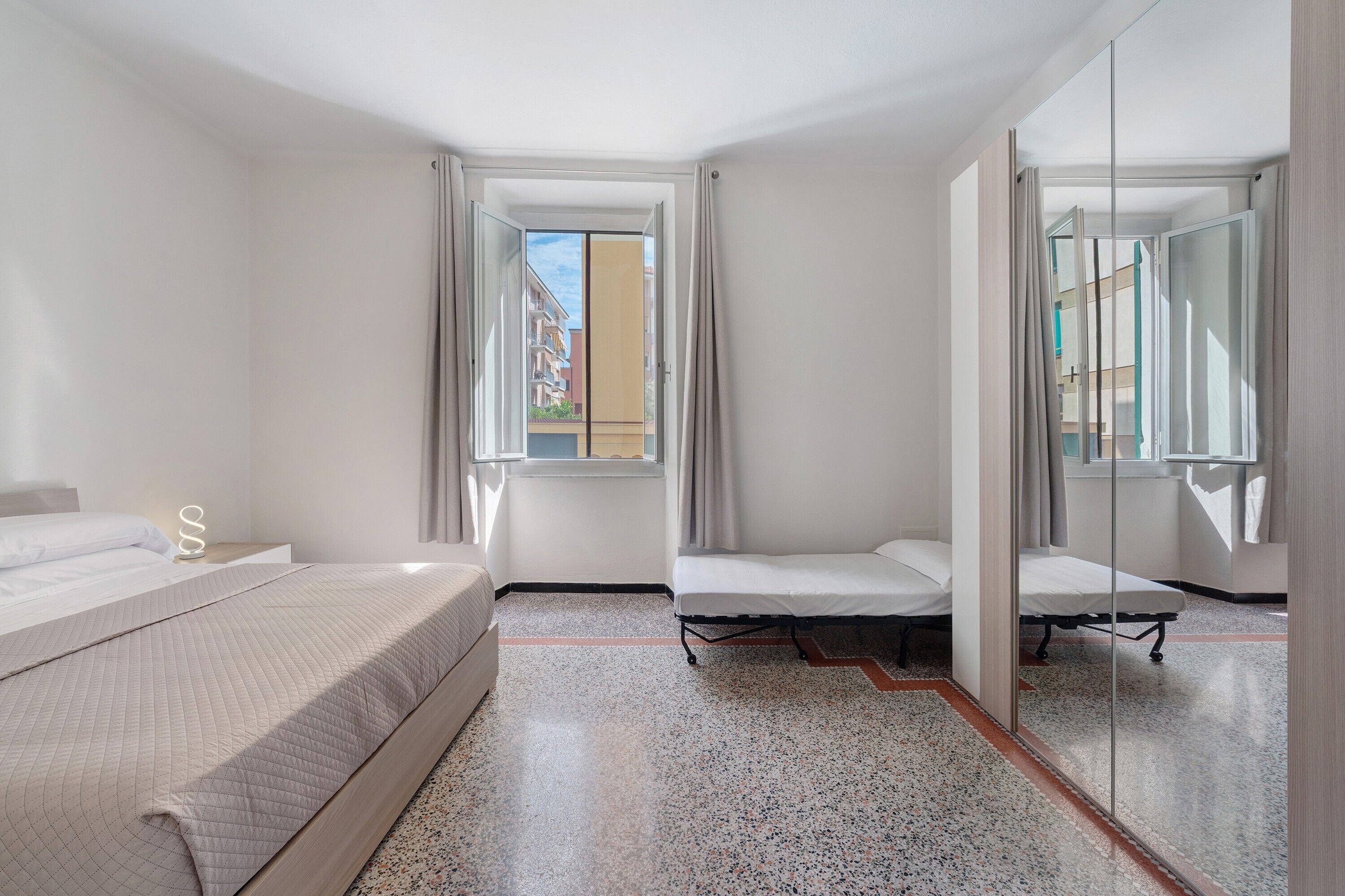 Una habitación de hotel con una cama, una mesita de noche pequeña, un espejo y una ventana.
