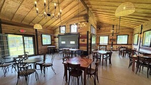 Ein geräumiger Innenbereich mit Essbereich, Holztischen und -stühlen, großen Fenstern und einer hohen Decke mit freiliegenden Balken.