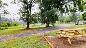 Taula de picnic en un paratge rural amb un camí de grava, arbres i un edifici al capvespre.