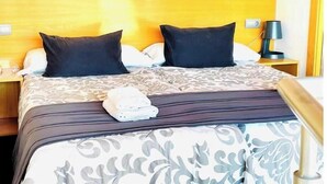 Une chambre d’hôtel avec un lit, deux oreillers, une lampe de chevet et une serviette pliée posée sur le lit.