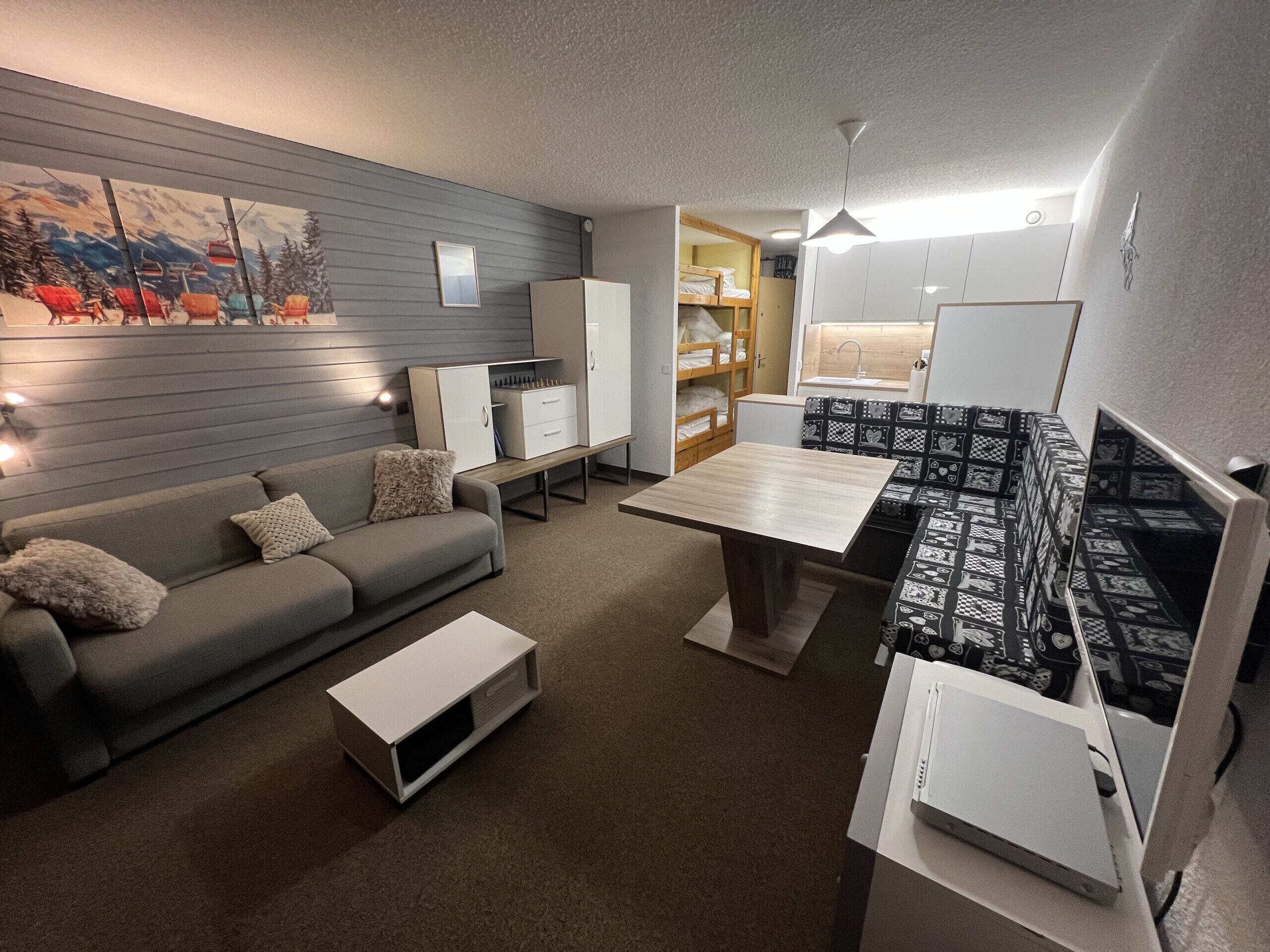 A compact living space with a sofa, a small table, a kitchenette, and a painting on the wall.