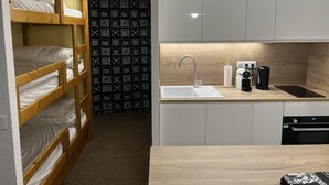 A compact kitchen with a sink, a coffee machine, and a toaster. There is a bunk bed with white bedding to the left.