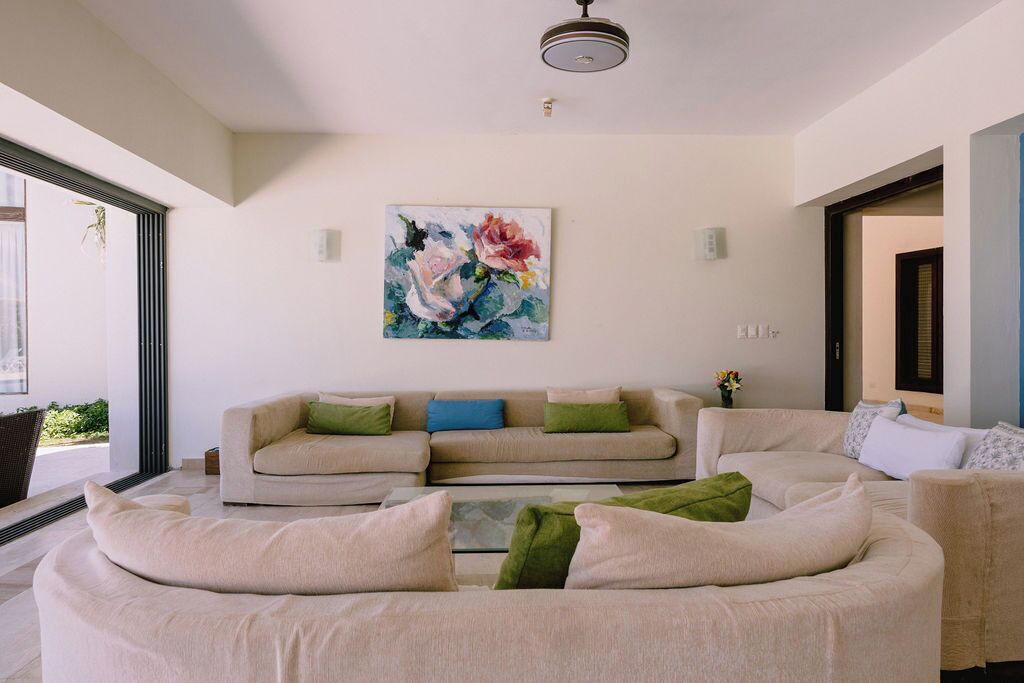 A modern living room with a beige sofa set, a coffee table, and a large floral painting on the wall.