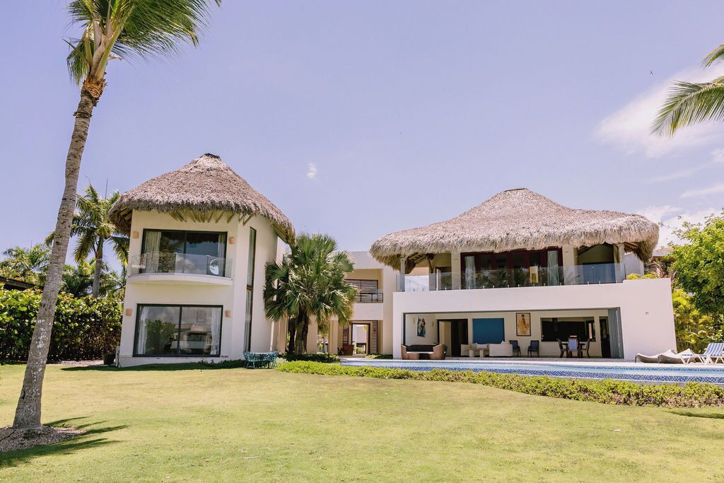 A resort with two buildings, each with a thatched roof, a pool, and a well-maintained lawn.