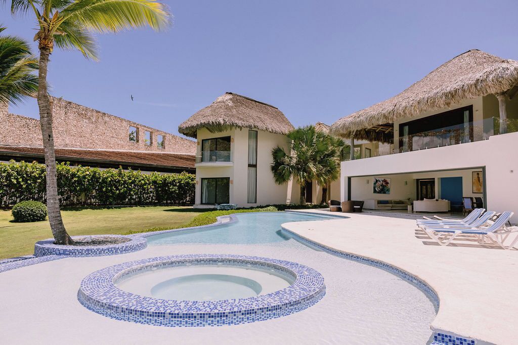 A resort with a swimming pool, thatched-roof buildings, and lounge chairs.