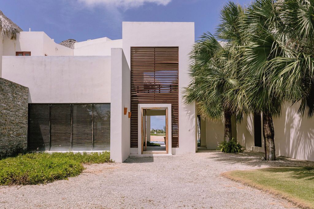 A modern building with a central entrance, a gravel pathway, and palm trees.