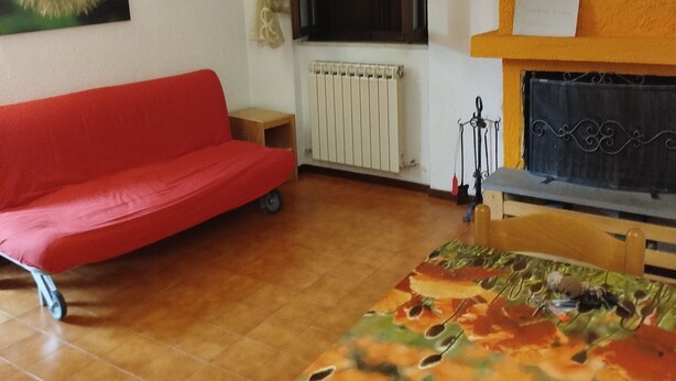 Una stanza con un divano rosso, un letto con copripiumino floreale, un termosifone, una finestra con tende e un camino.