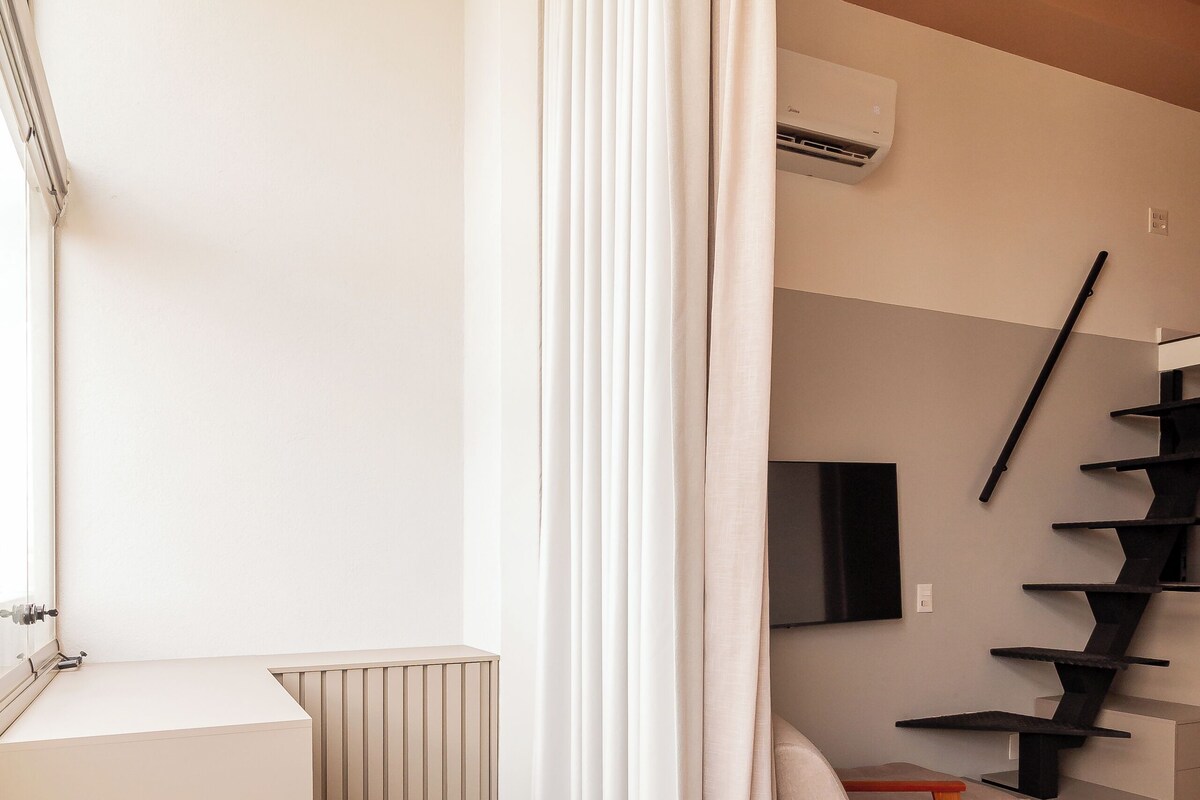 A modern, minimalist room with a white table, a chair, a radiator, and a staircase.