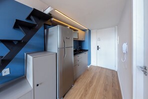 A modern kitchen with a stainless steel refrigerator, a microwave, and a built-in oven. There is a wooden floor and a blue accent wall. - Arapanes by Bhomy (São Paulo)