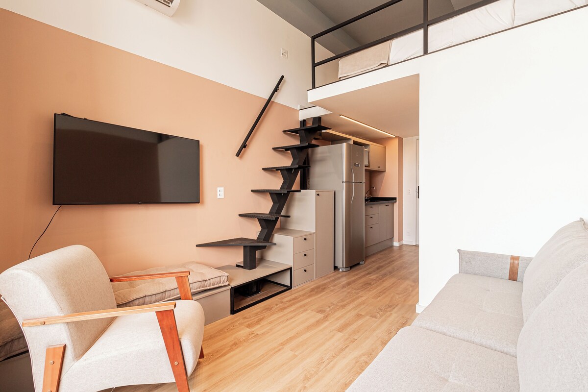 A modern living space with a flat-screen TV mounted on the wall, a sofa, a wooden coffee table, and a staircase leading to an upper level.