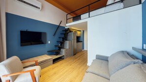 A compact living space with a sofa, a chair, a TV, a staircase leading to a kitchen, and a bunk bed. - Arapanes by Bhomy (São Paulo)