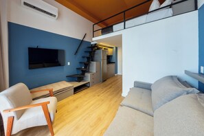 A compact living space with a sofa, a chair, a TV, a staircase leading to a kitchen, and a bunk bed. - Arapanes by Bhomy (São Paulo)