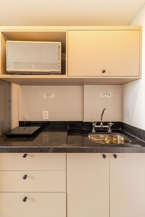 A compact kitchen with a built-in microwave, a sink with a modern faucet, and a countertop with a black granite finish. - Arapanes by Bhomy (São Paulo)