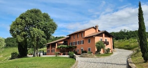 Ein großes, zweistöckiges Haus mit einem steinernen Weg, der zum Eingang führt, umgeben von üppiger Bepflanzung und Bäumen.