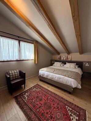 Ein Schlafzimmer mit einem Bett, einem Sessel, einem Teppich und Holzbalken an der Decke.