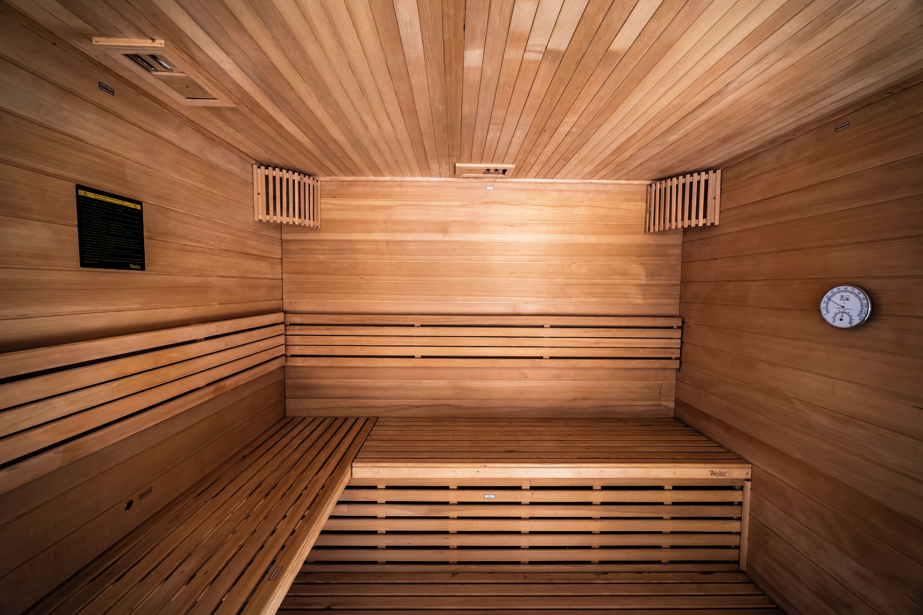 Eine Sauna mit Holzlamellen an Wänden und Decke, einer Sitzbank und einem Temperaturanzeiger.