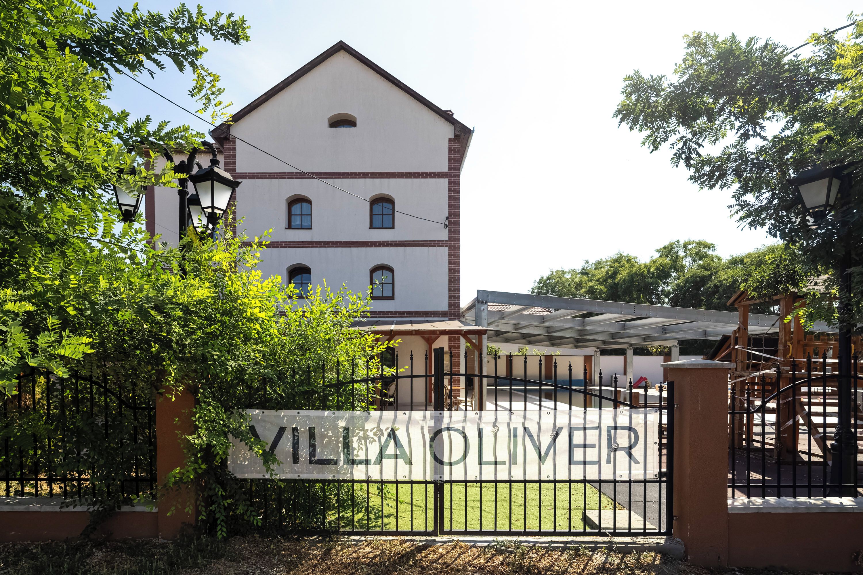Villa Oliver with a gated entrance, a white building with a red roof, and a clear sky.