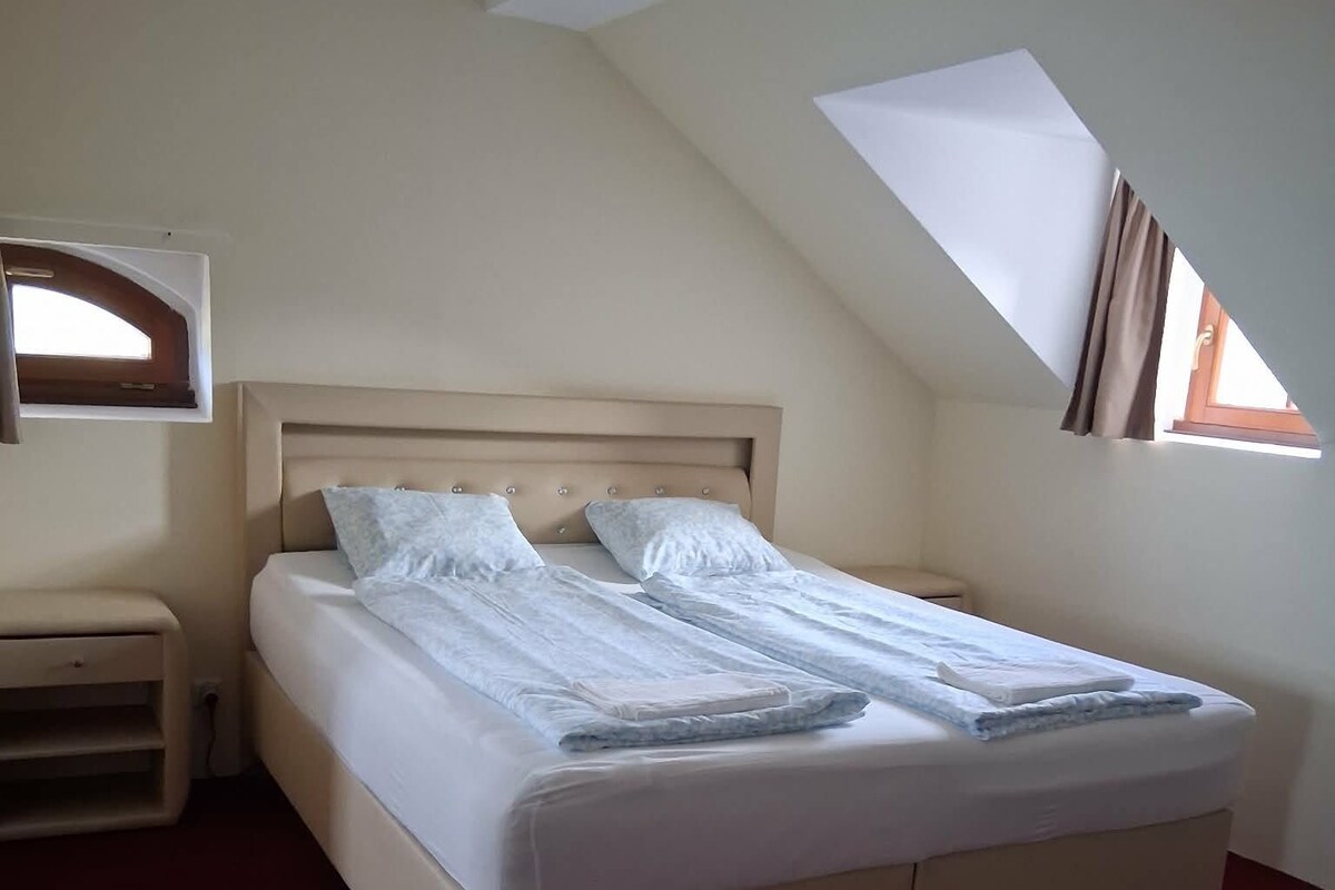 A single bed with a headboard, a bedside table, and a window with curtains.