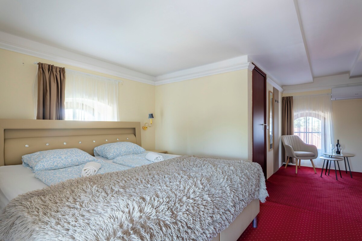 Habitación de hotel con una cama grande, una silla, una mesita y una ventana con cortinas.