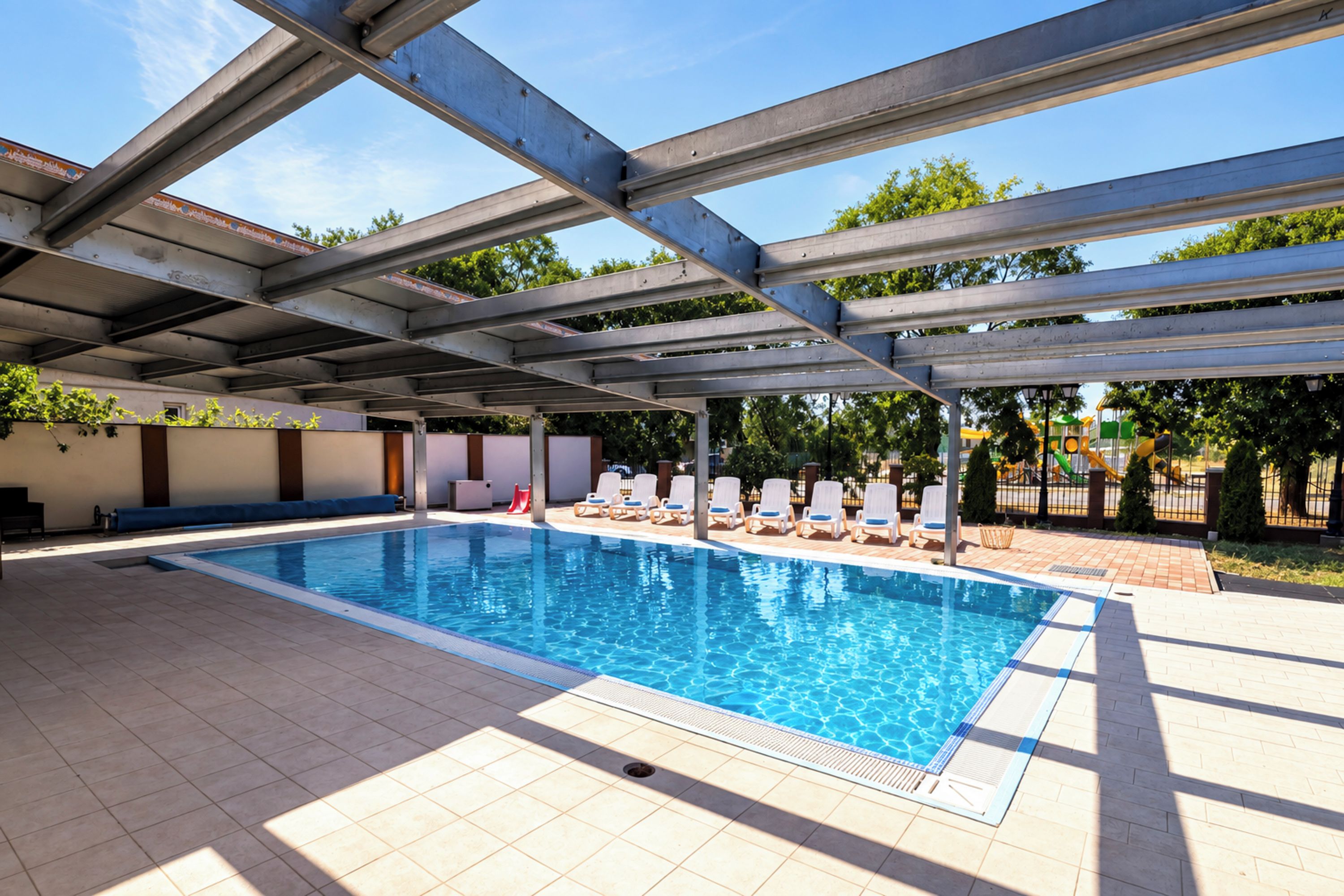 A swimming pool with a covered area, lounge chairs, and a tiled deck.