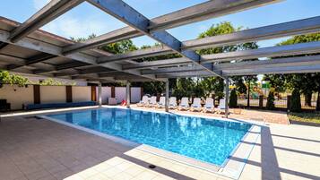 A swimming pool with a covered area, lounge chairs, and a tiled deck.