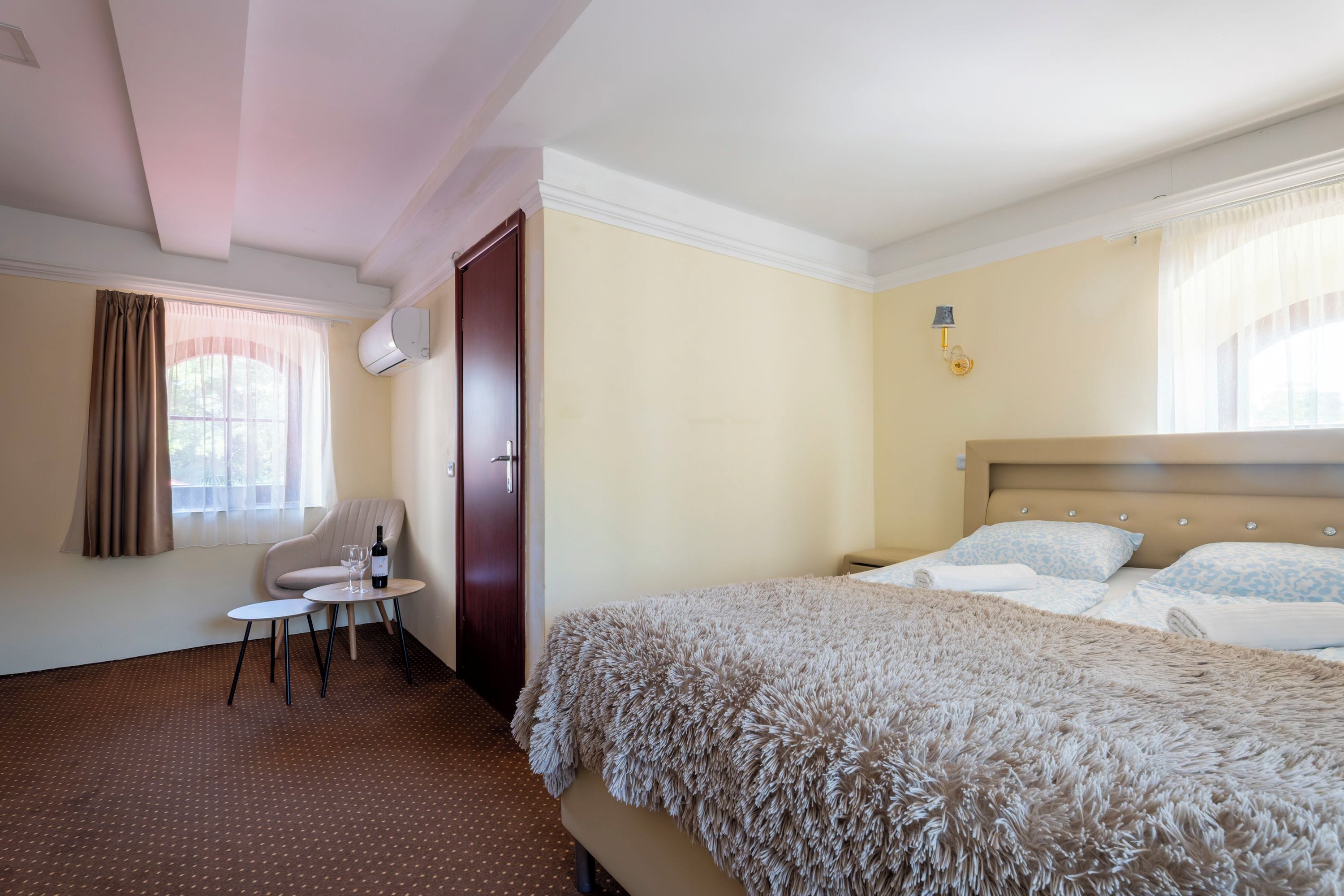 A hotel room with a bed, a chair, a small table, and a window with curtains.