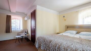 A hotel room with a bed, a chair, a small table, and a window with curtains.