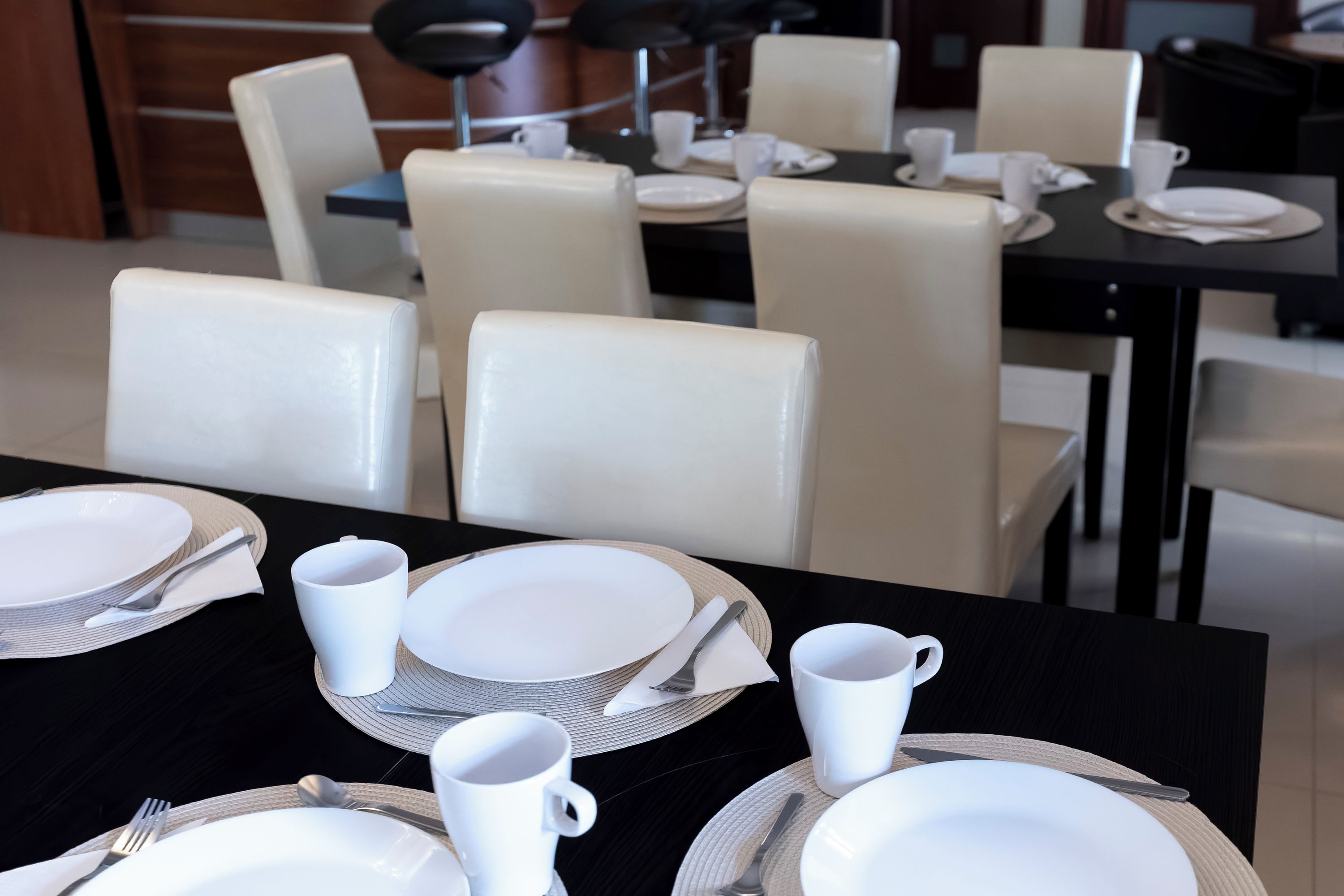 A dining area with tables set for four, each with white plates, cutlery, and cups.