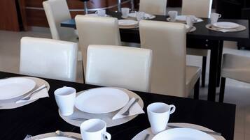 A dining area with tables set for four, each with white plates, cutlery, and cups.