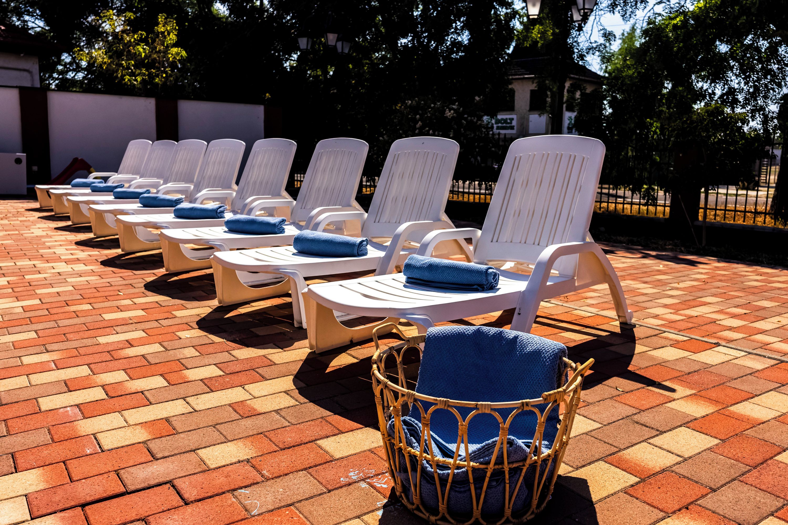 A row of white lounge chairs with blue towels, arranged on a brick patio.