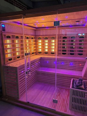 A sauna with wooden benches and glass walls, featuring a control panel and a small rock display. - Villa Oliver Abádszalók (Abádszalók)