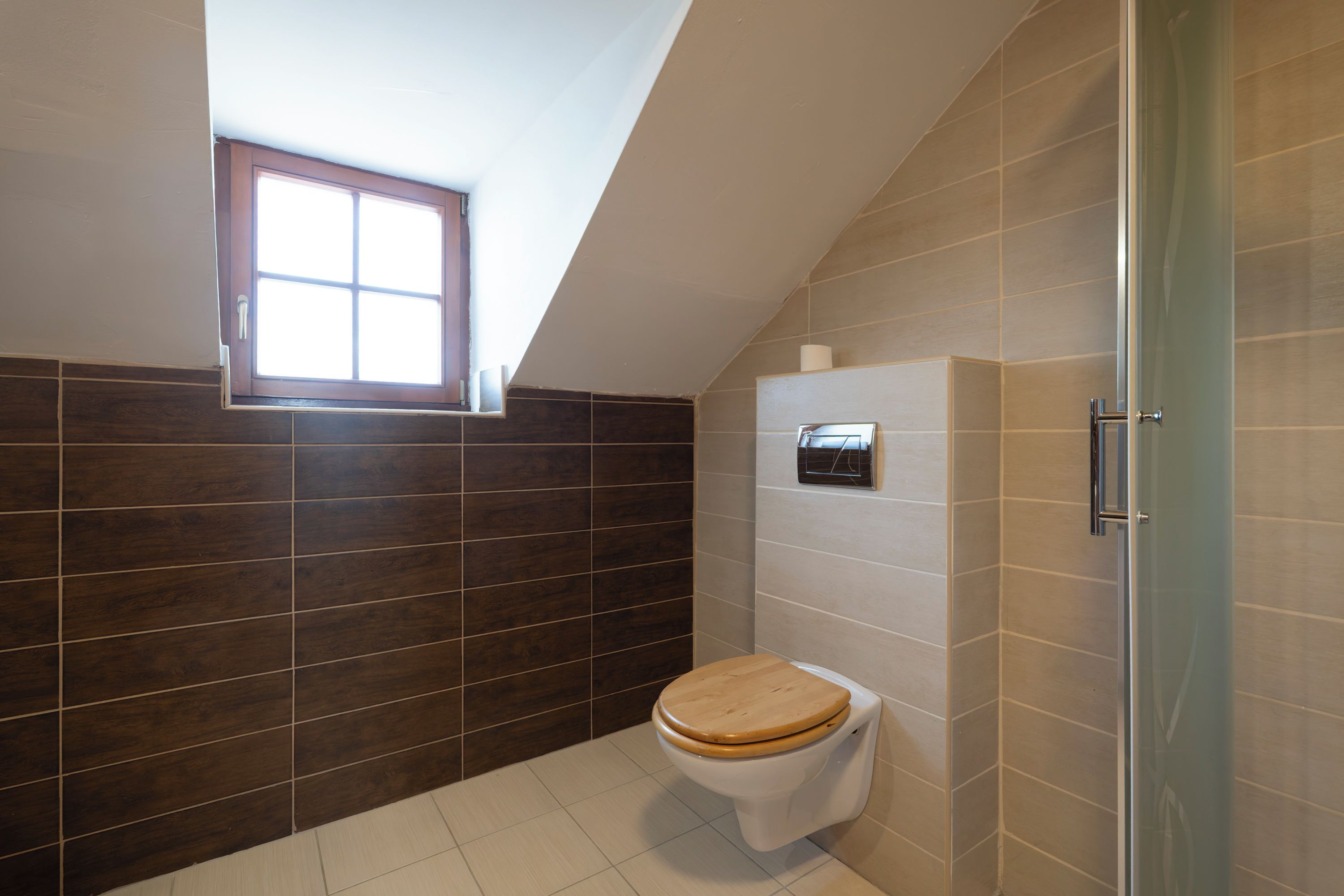 A bathroom with a wooden toilet, a window, and a shower area.