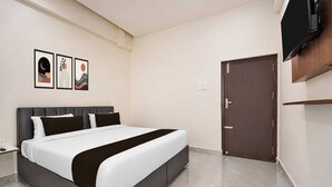 A modern hotel room with a large bed, a flat-screen TV mounted on the wall, and a door with a handle. - Deluxe Twin Clubhouse Vytilla Kochi (Kanayannur)