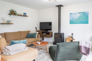 A living room with a sofa, a coffee table, a TV, a fireplace, and a painting on the wall. - Sea Side Village 91* (De Haan)