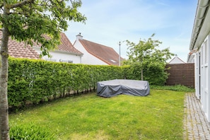 A residential backyard with a covered outdoor table, a well-maintained hedge, and a house with a red-tiled roof. - Sea Side Village 91* (De Haan)