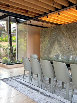 Un espace de salle à manger moderne avec une table en verre, six chaises, un mur en marbre et un plafond en bois.